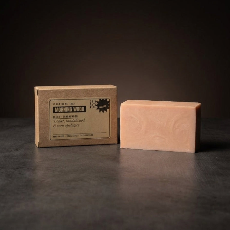 A rectangular bar of soap in a pale peach-pink color stands next to its cardboard packaging box on a dark, reflective surface against a dark background.